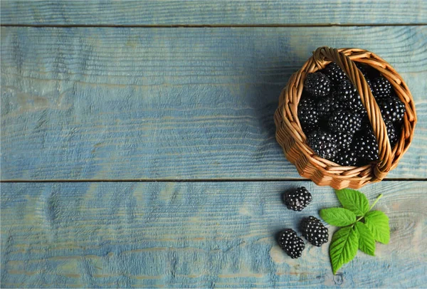 Wicker basket of tasty blackberries and leaves on blue wooden table, flat lay. Space for text — Stock Photo, Image