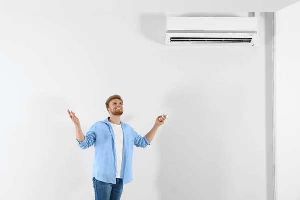 Junger Mann bedient Klimaanlage mit Fernbedienung in Innenräumen. Raum für Text — Stockfoto