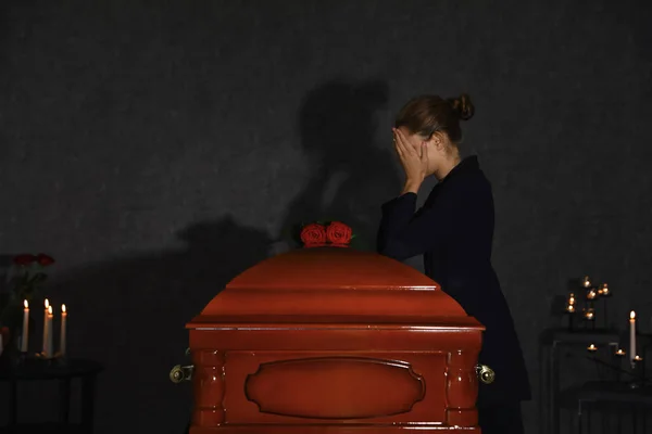 Triste jeune femme en deuil près du cercueil funéraire avec des roses rouges dans la chapelle — Photo