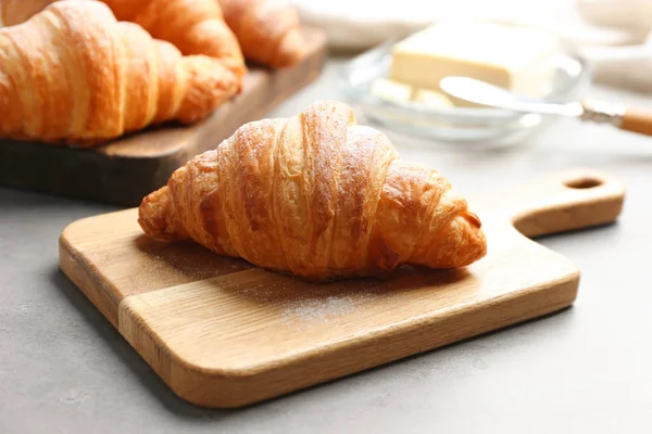 Tablero de madera con sabroso croissant sobre mesa gris. Pastelería francesa — Foto de Stock