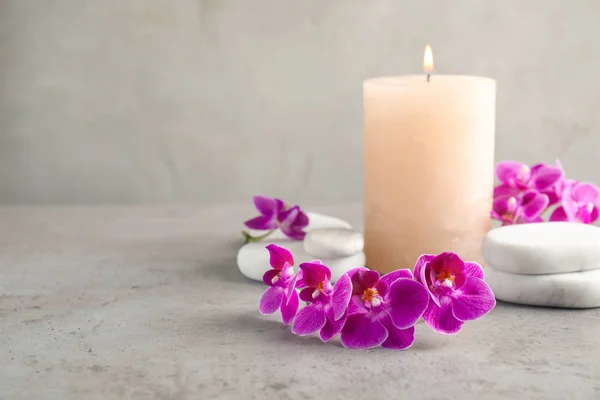 Fleurs d'orchidée, pierres de spa et bougie sur la table grise. Espace pour le texte — Photo