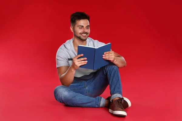 Yakışıklı genç adam kırmızı arka plan kitap okuma — Stok fotoğraf