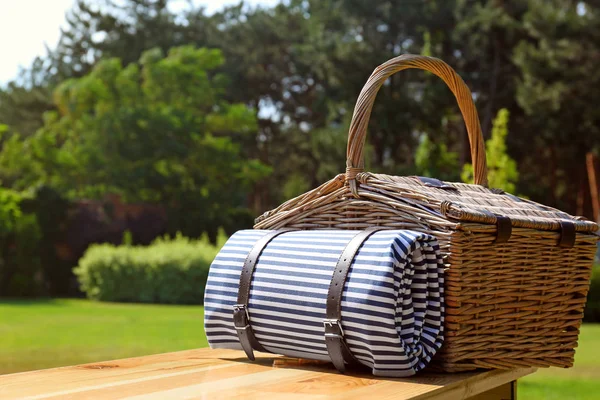 Picknickmand met deken op houten tafel in groen park — Stockfoto