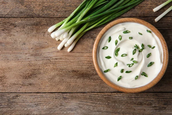 Tigela de creme azedo fresco com cebola verde na mesa de madeira, flat lay. Espaço para texto — Fotografia de Stock