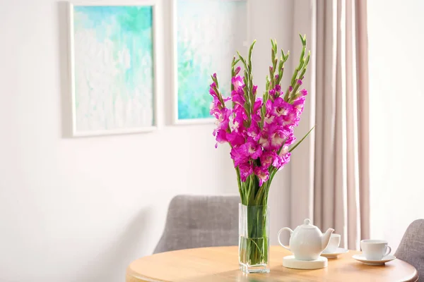 Vase avec de belles fleurs de gladiolus roses et un ensemble de thé sur une table en bois dans la chambre, espace pour le texte — Photo