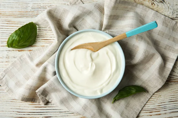 Bowl of sour cream with spoon and napkin on white wooden table, flat lay — Stock Photo, Image