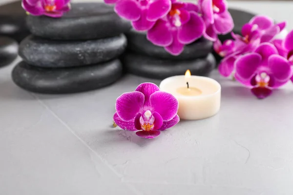 Pierres de spa, fleurs d'orchidée et bougie sur fond gris — Photo