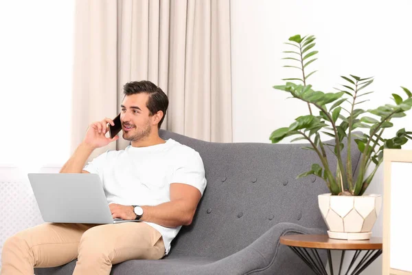 Guapo joven hablando por teléfono mientras trabaja con el ordenador portátil en el interior —  Fotos de Stock