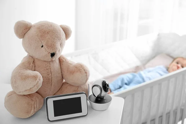 Babyfon, Kamera und Spielzeug auf dem Tisch neben dem Kinderbett mit Kind im Zimmer. Video-Kindermädchen — Stockfoto
