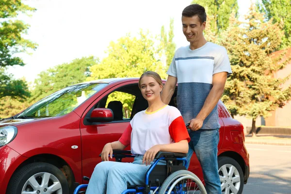 Jonge man met gehandicapte vrouw in rolstoel in de buurt van auto buitenshuis — Stockfoto