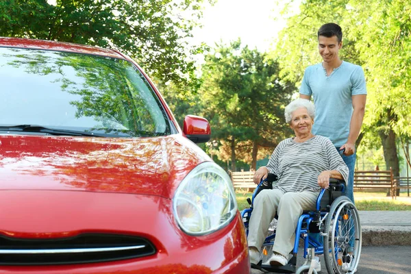 Młody mężczyzna z niepełnosprawnym starszym kobietą na wózku w pobliżu samochodu na zewnątrz — Zdjęcie stockowe