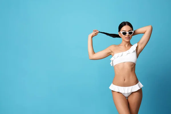 Hermosa joven en bikini blanco con gafas de sol sobre fondo azul claro. Espacio para texto —  Fotos de Stock