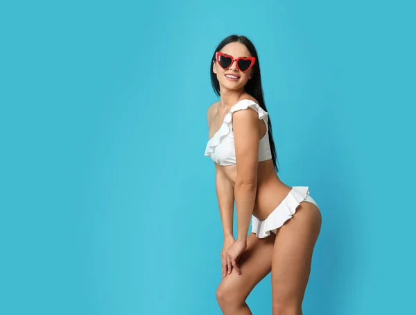 Mooie jonge vrouw in witte bikini met zonnebril op licht blauwe achtergrond. Ruimte voor tekst — Stockfoto