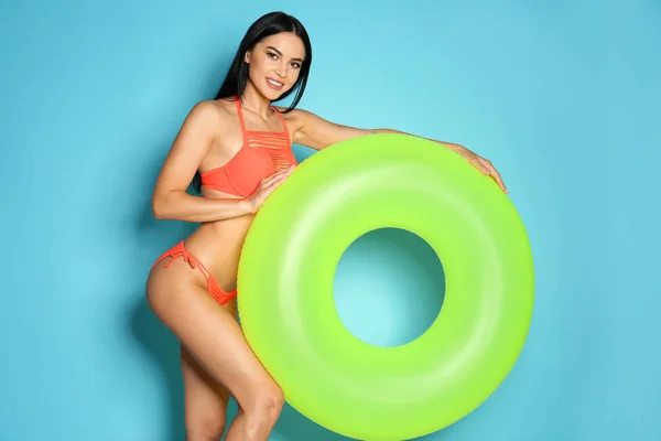 Belle jeune femme en bikini élégant avec anneau gonflable vert sur fond bleu clair — Photo