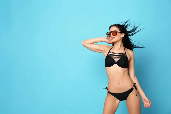 stock image Beautiful young woman in stylish bikini with sunglasses on light blue background. Space for text