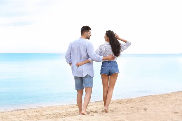 Feliz joven pareja caminando juntos en la playa cerca del mar — Foto de Stock