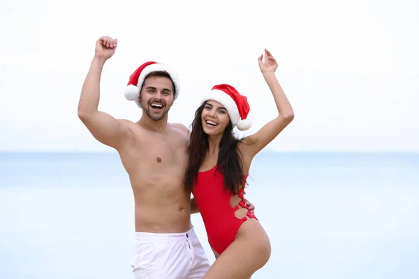 Feliz pareja joven con sombreros de Santa juntos en la playa — Foto de Stock