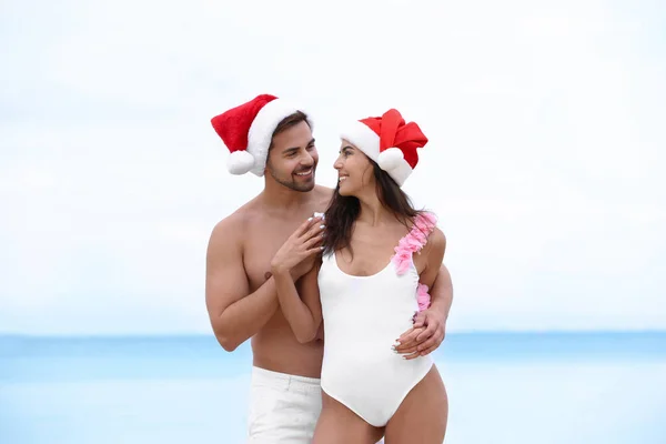 Joyeux jeune couple avec chapeaux de Père Noël ensemble sur la plage — Photo