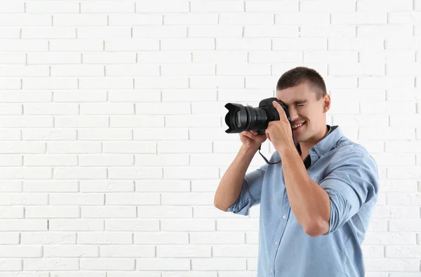 Jovem fotógrafo profissional tirando fotos perto da parede de tijolo. Espaço para texto — Fotografia de Stock