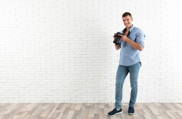 Fiatal fotós professzionális kamerával közel téglafal. Szóköz a szöveghez — Stock Fotó