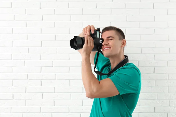 Jovem fotógrafo profissional tirando fotos perto da parede de tijolo. Espaço para texto — Fotografia de Stock