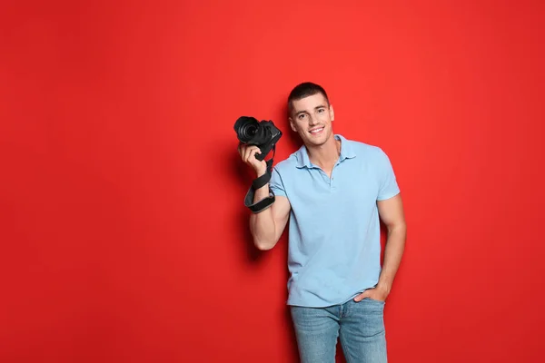 Mladý fotograf s profesionálním fotoaparátem na červeném pozadí. Místo pro text — Stock fotografie