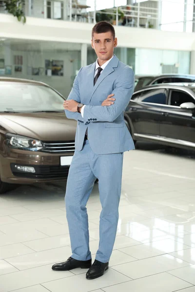 Jonge verkoper in de buurt van nieuwe auto in modern dealer — Stockfoto