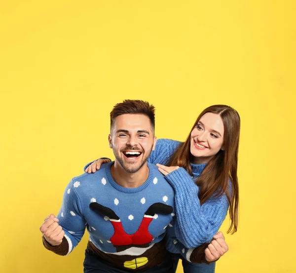 Pareja vistiendo suéteres de Navidad sobre fondo amarillo — Foto de Stock