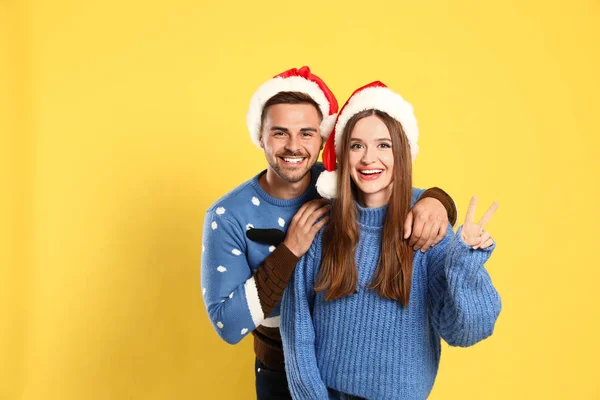 Paar trägt Weihnachtspullover und Weihnachtsmützen auf gelbem Hintergrund — Stockfoto