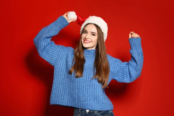 Jovem mulher em camisola de Natal e chapéu de Papai Noel no fundo vermelho — Fotografia de Stock