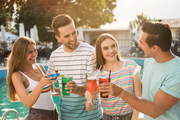 Mutlu genç arkadaşlar taze yaz kokteylleriyle yüzme havuzunun yanında dinleniyorlar.