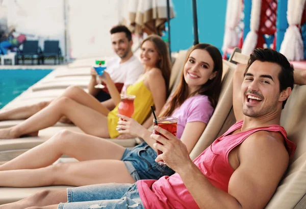 Felices jóvenes amigos con cócteles frescos de verano relajándose en tumbonas cerca de la piscina — Foto de Stock