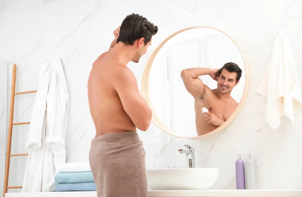 Handsome young man applying deodorant in bathroom