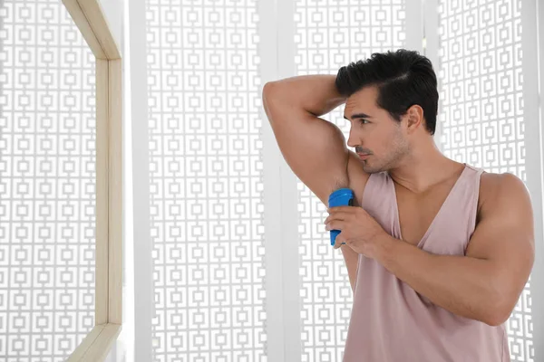 Handsome young man applying deodorant in bathroom. Space for text