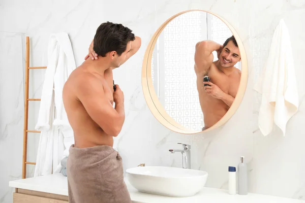 Beau jeune homme appliquant déodorant dans salle de bain — Photo