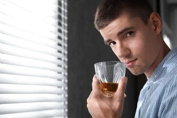 Jeune homme avec un verre de whisky près de la fenêtre à l'intérieur. Espace pour le texte — Photo