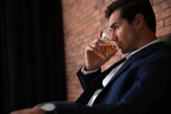 Jeune homme avec un verre de whisky près du mur de briques à l'intérieur. Espace pour le texte — Photo