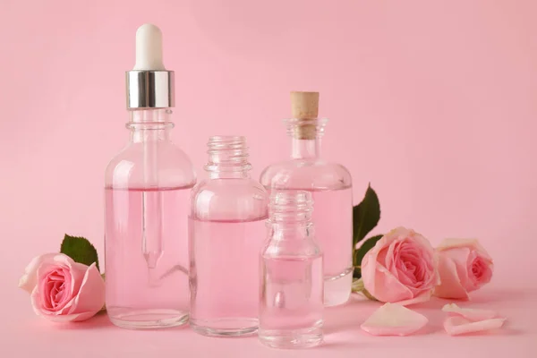 Botellas de aceite esencial y rosas sobre fondo rosa —  Fotos de Stock