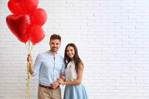 Young couple with air balloons near white brick wall. Celebration of Saint Valentine's Day — Stock Photo, Image