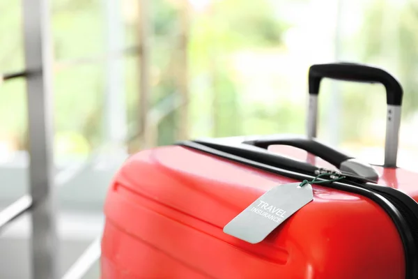 Stylischer Koffer mit Reiseversicherungsetikett auf verschwommenem Hintergrund, Nahaufnahme. Raum für Text — Stockfoto