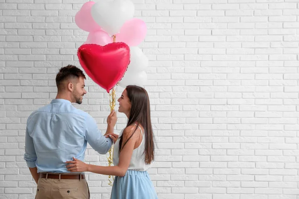 Mladý pár se vzduchovými balónky poblíž bílé cihlové zdi. Oslava svatého Valentýna — Stock fotografie