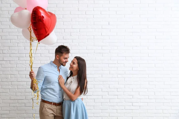 Pareja joven con globos de aire cerca de la pared de ladrillo blanco. Celebración del Día de San Valentín — Foto de Stock