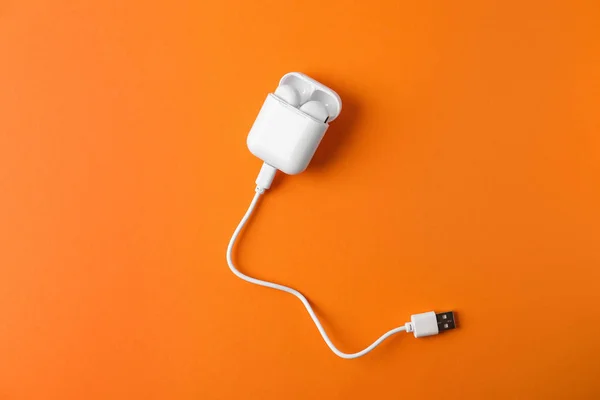 Modern wireless earphones in charging case with cable on orange background, top view