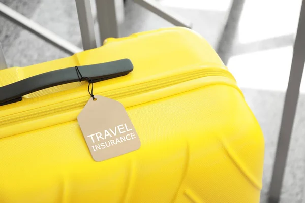 Żółta walizka z etykietą ubezpieczenia podróżnego na schodach w pomieszczeniu, zbliżenie — Zdjęcie stockowe