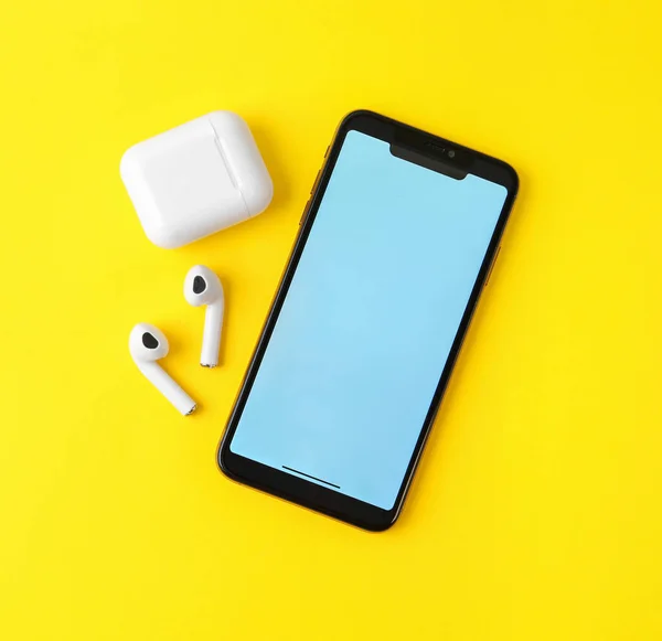 Fones de ouvido sem fio, telefone celular e estojo de carregamento em fundo amarelo, flat lay. Espaço para texto — Fotografia de Stock