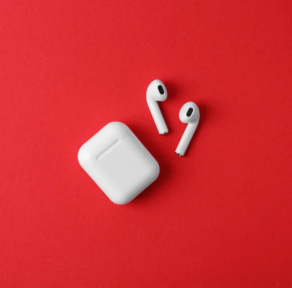 Modern wireless earphones and charging case on red background, flat lay — Stock Photo, Image