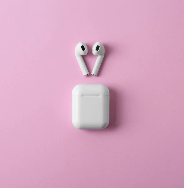 Fones de ouvido sem fio modernos e caixa de carregamento em fundo rosa, flat lay — Fotografia de Stock