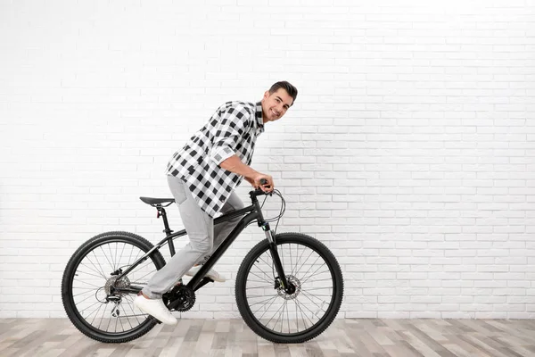 Pohledný mladý muž s moderním bicyklem blízko bílé cihlové zdi uvnitř — Stock fotografie