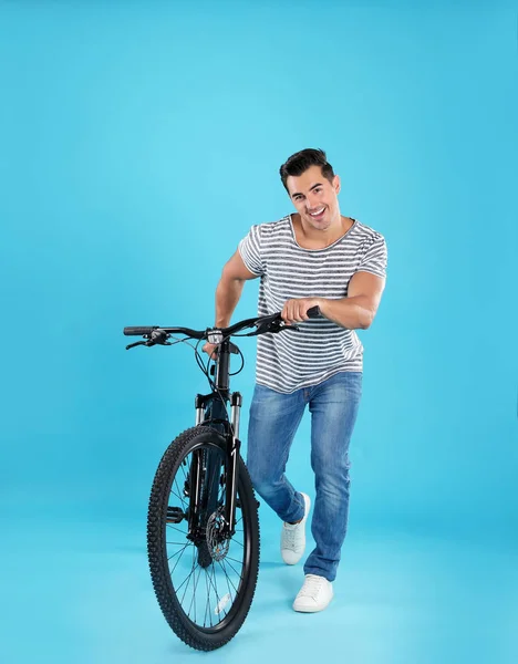 Schöner junger Mann mit modernem Fahrrad auf hellblauem Hintergrund — Stockfoto