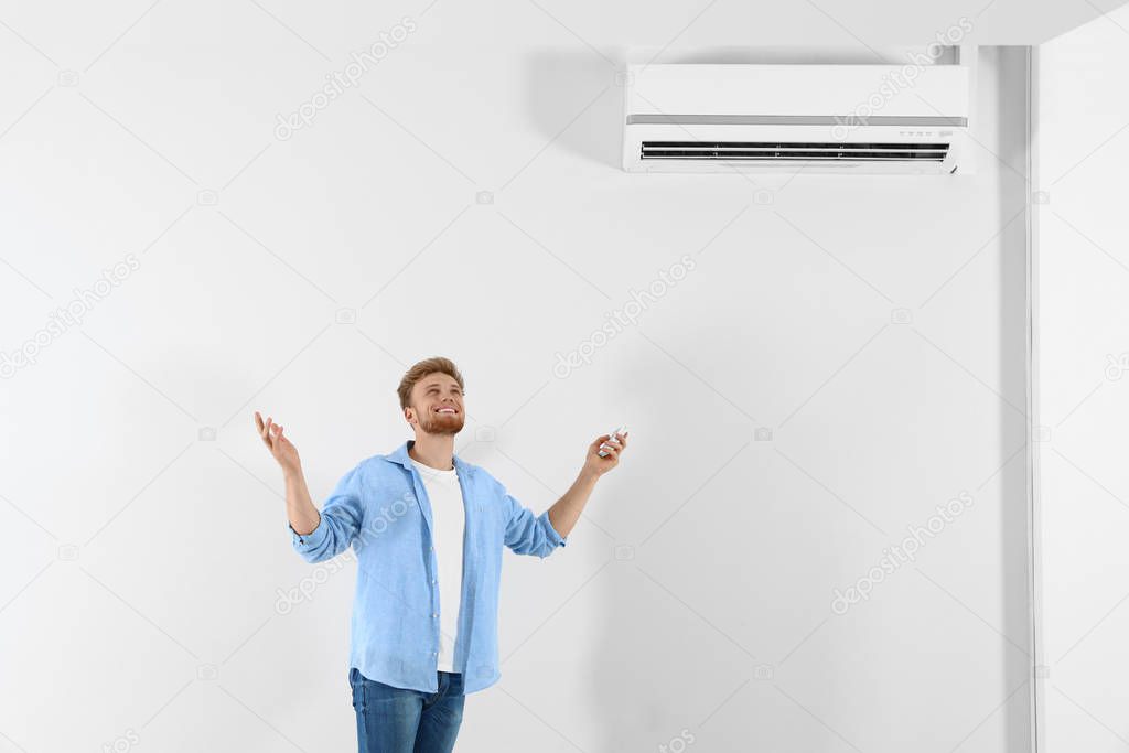 Young man operating air conditioner with remote control indoors. Space for text